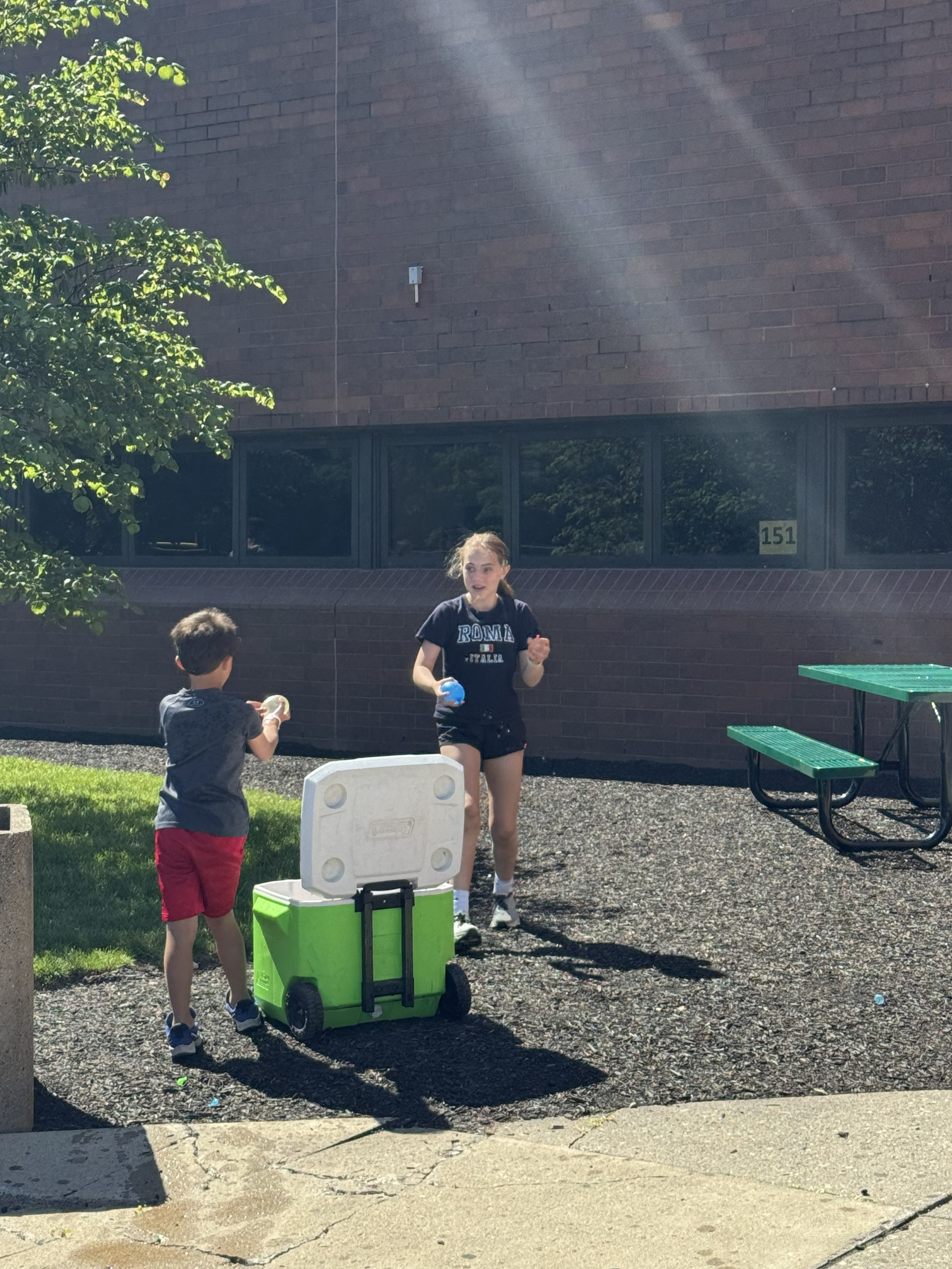 Two campers tossing a water balloon near a cooler