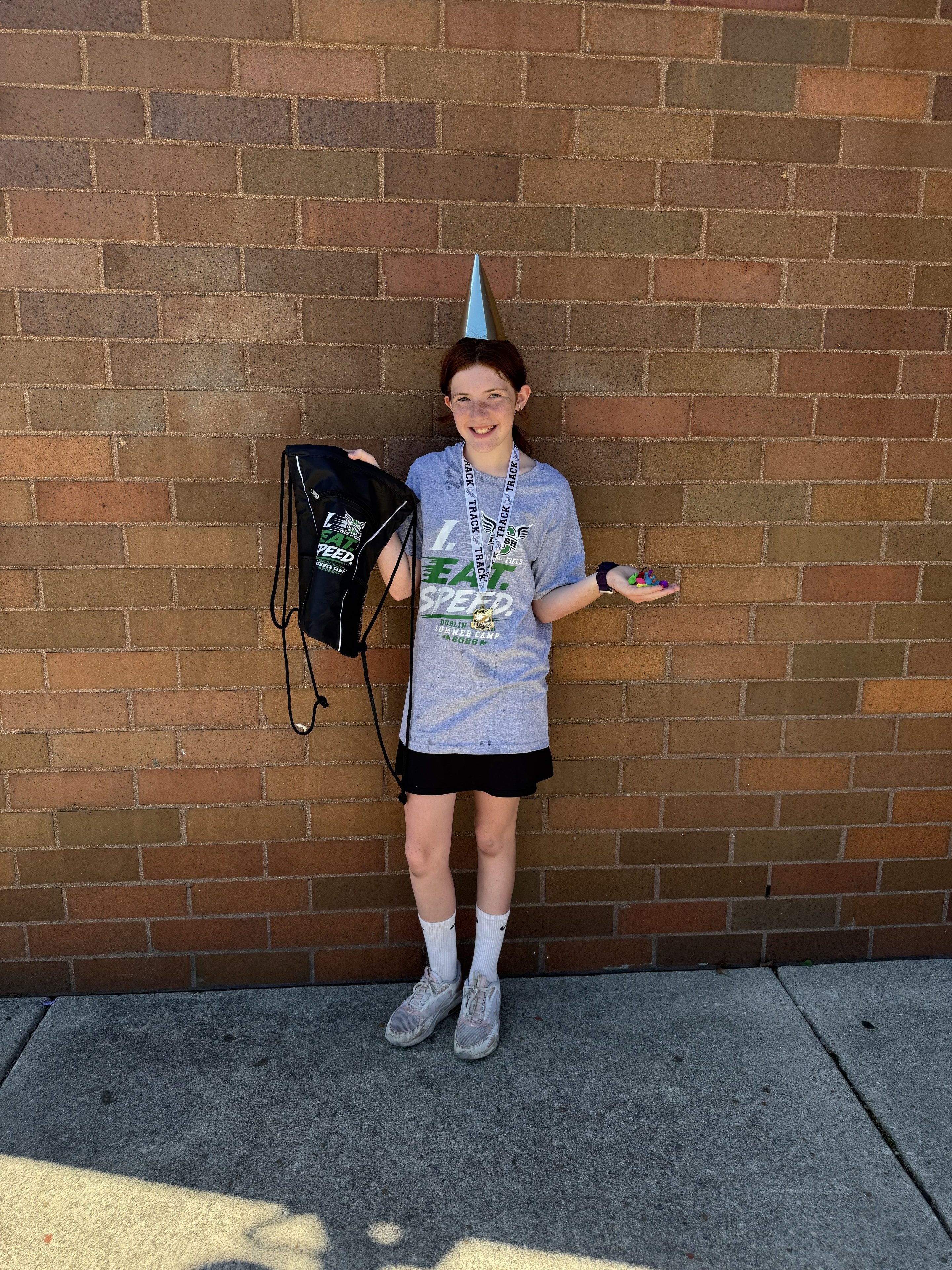 Camper in summer camp shirt and party hat holding her prize bag