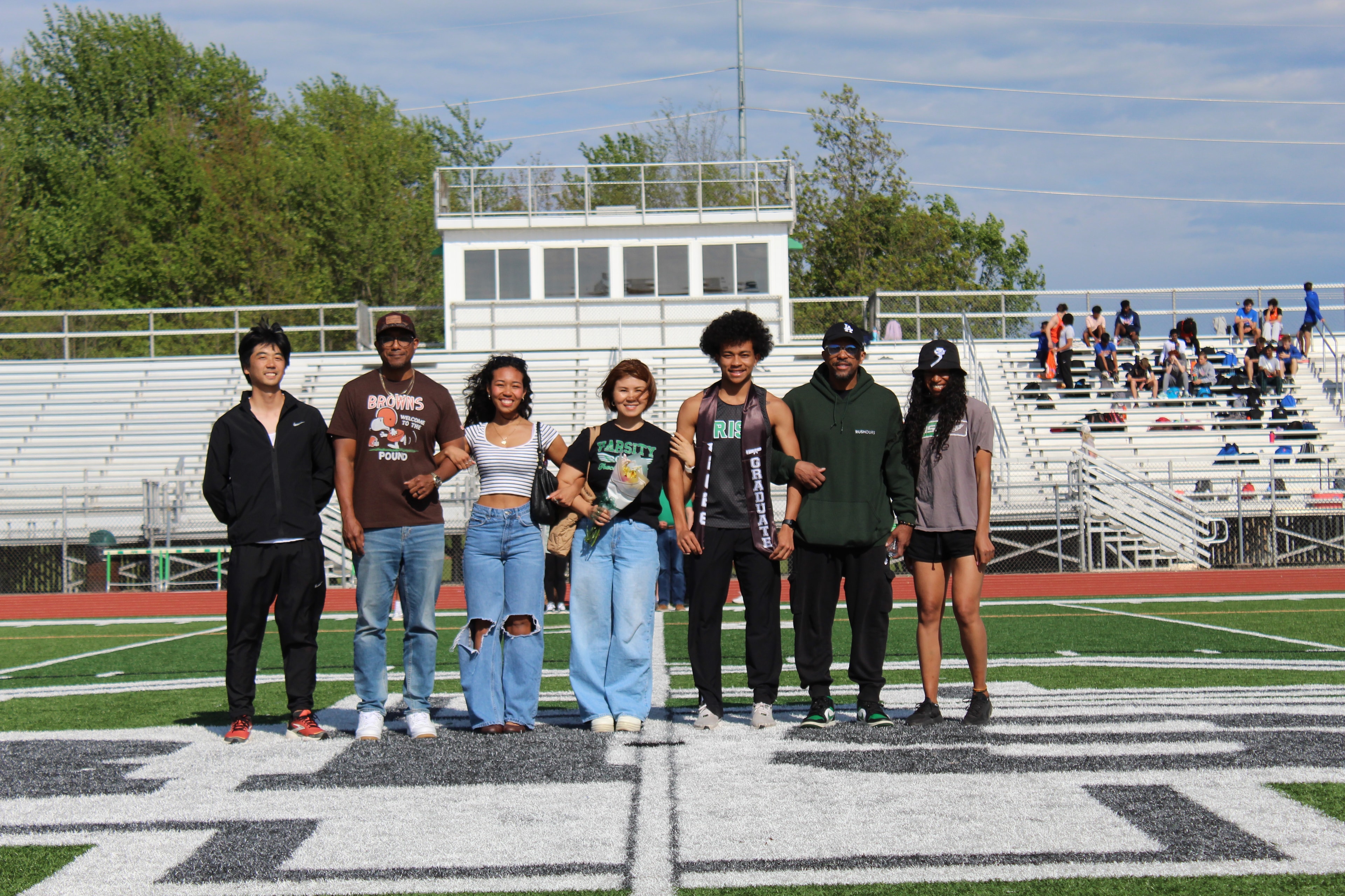 Senior in graduation sash with family on the field