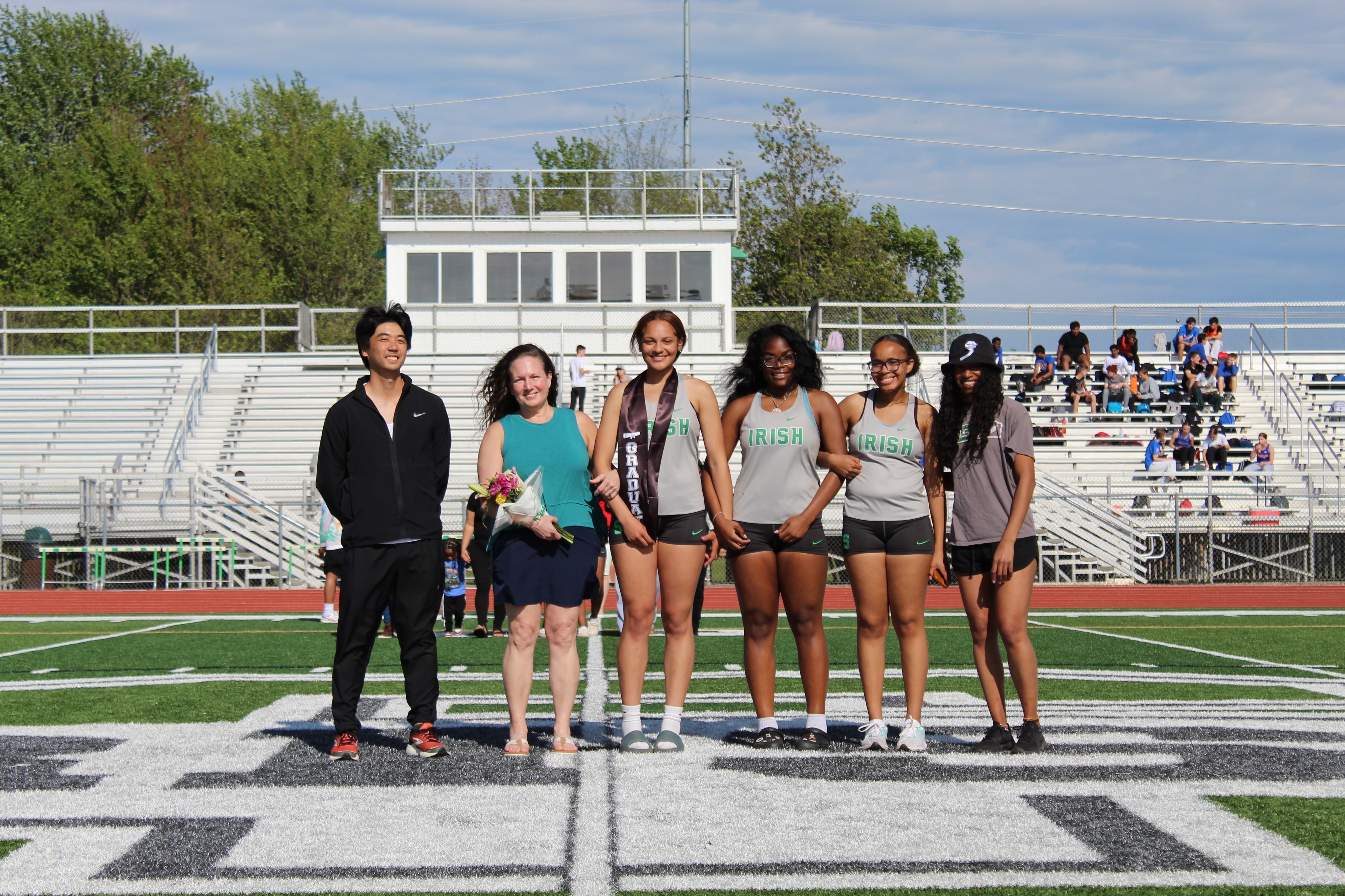 Senior girl in graduation sash with teammates in Irish uniforms on the field