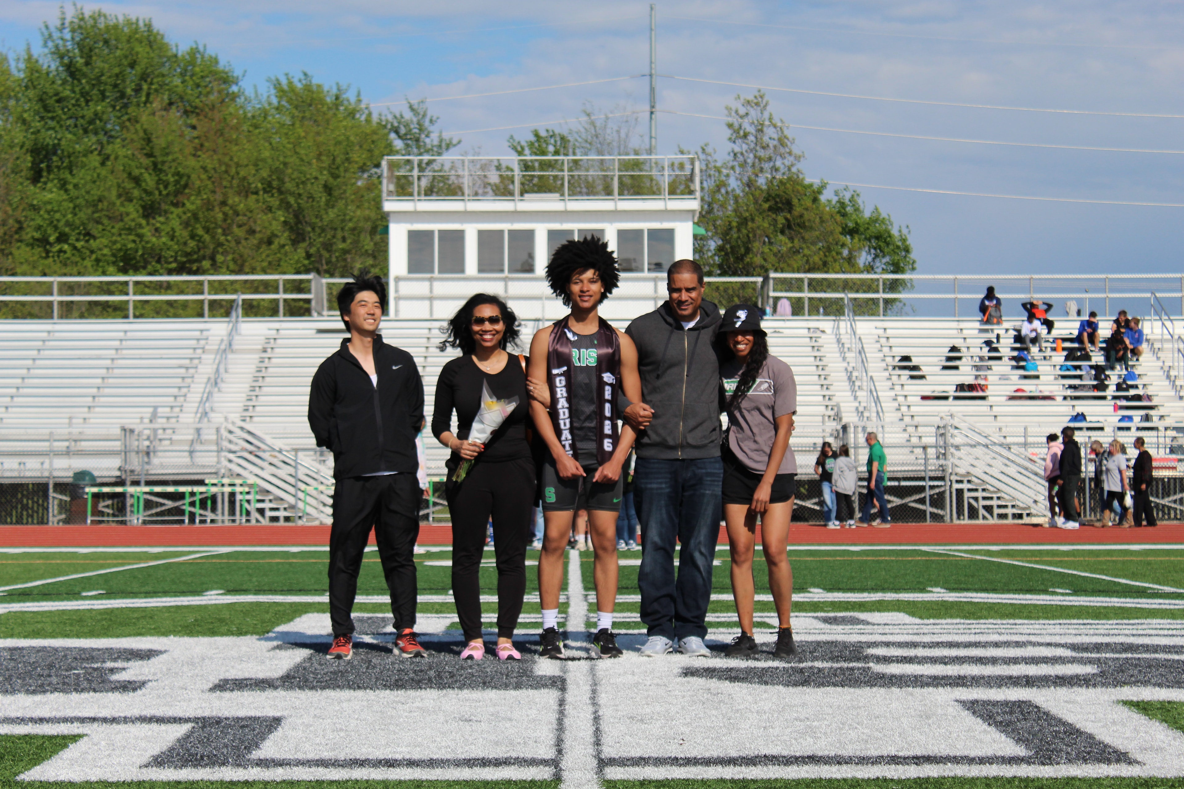 Senior in graduation sash with family on the field