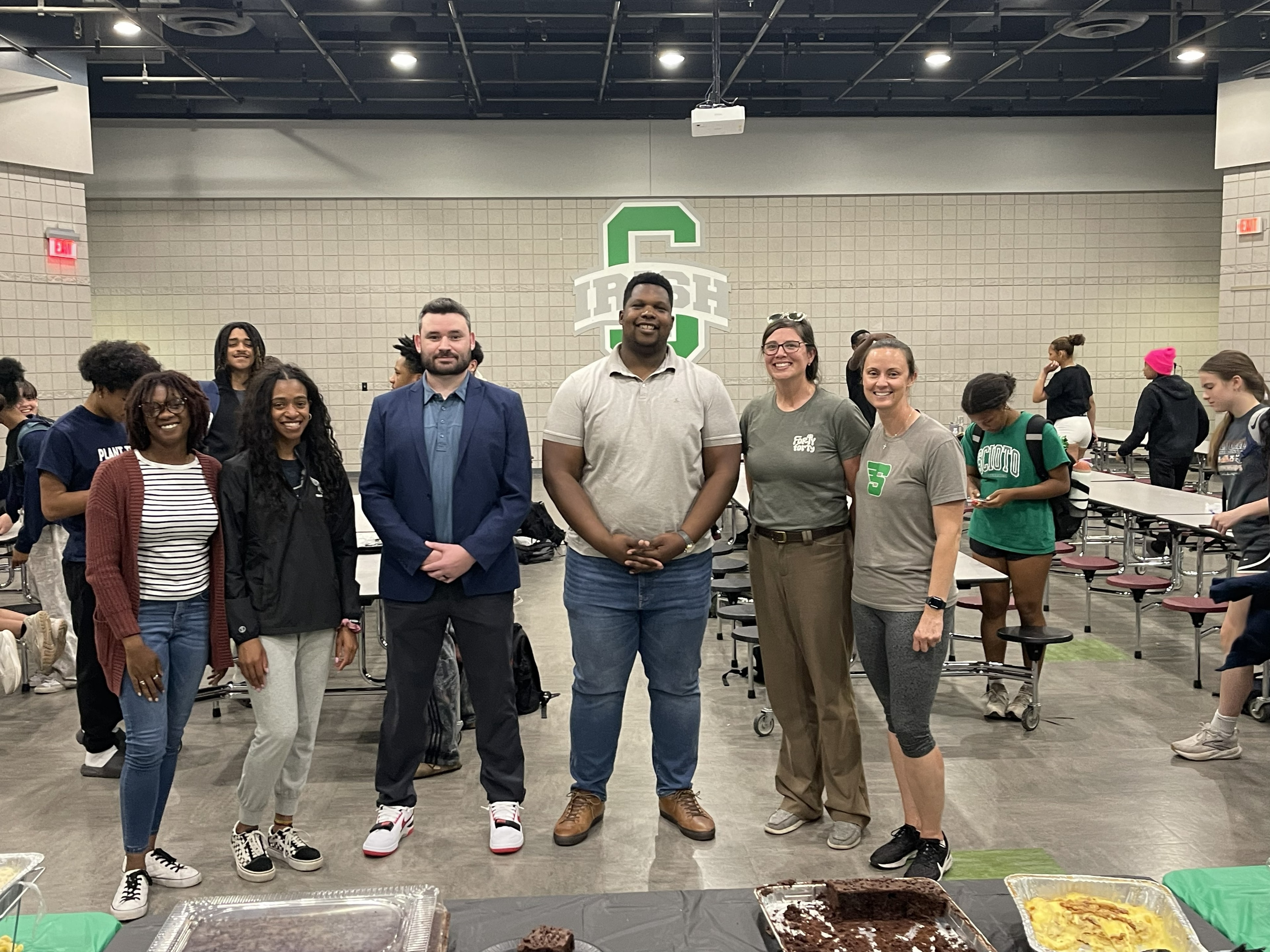 Coaches and athletes posing together in front of the Scioto Irish logo